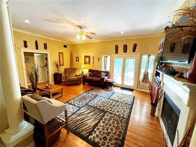 living room featuring a fireplace, a ceiling fan, light wood finished floors, decorative columns, and crown molding