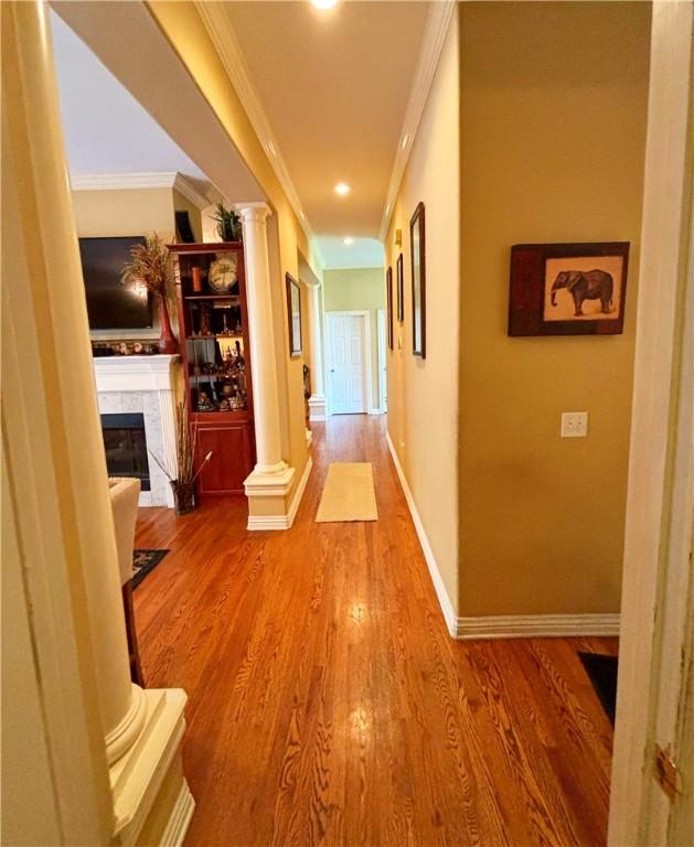 corridor with ornate columns, baseboards, ornamental molding, and wood finished floors