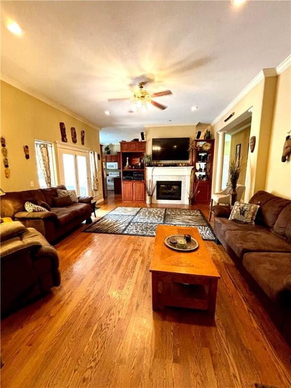 living room featuring crown molding, a ceiling fan, wood finished floors, and a glass covered fireplace