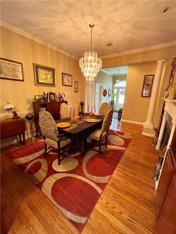 dining area with wood finished floors, an inviting chandelier, crown molding, ornate columns, and a fireplace