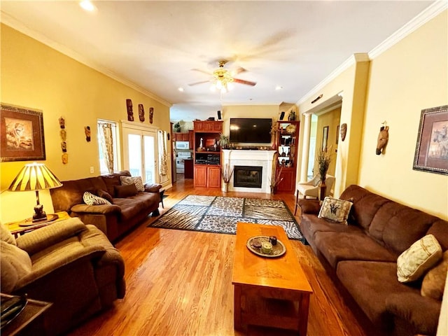 living area with recessed lighting, wood finished floors, a ceiling fan, ornamental molding, and a glass covered fireplace