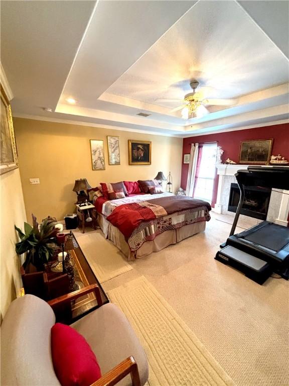 carpeted bedroom with ceiling fan, a tray ceiling, and a premium fireplace