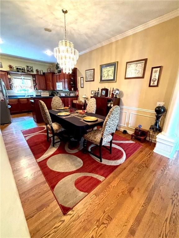 dining room featuring a wainscoted wall, ornamental molding, wood finished floors, a decorative wall, and a notable chandelier