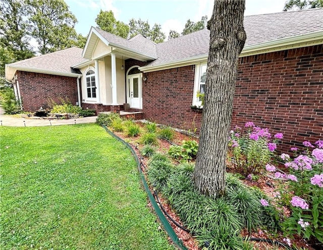 view of front facade featuring a shingled roof, a front yard, brick siding, and stucco siding