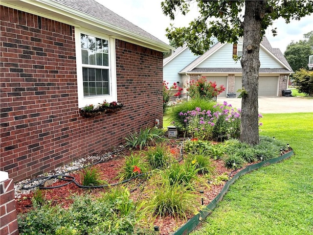 view of side of home featuring brick siding, a shingled roof, an outdoor structure, driveway, and a lawn