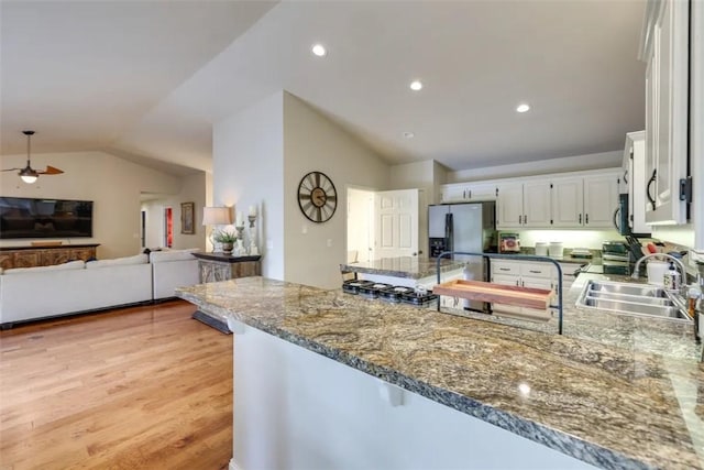 kitchen featuring stainless steel fridge with ice dispenser, vaulted ceiling, a sink, a peninsula, and open floor plan