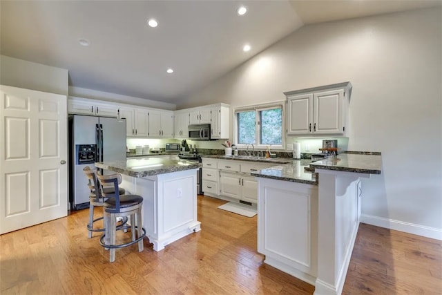 kitchen with dark stone countertops, kitchen peninsula, appliances with stainless steel finishes, a breakfast bar area, and light hardwood / wood-style floors