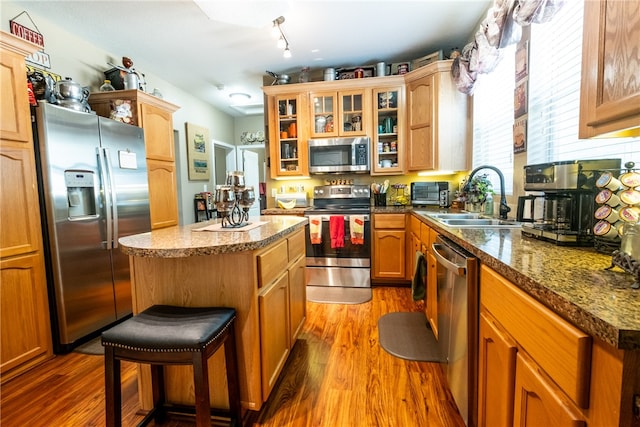 kitchen featuring a kitchen breakfast bar, wood-type flooring, appliances with stainless steel finishes, a center island, and sink