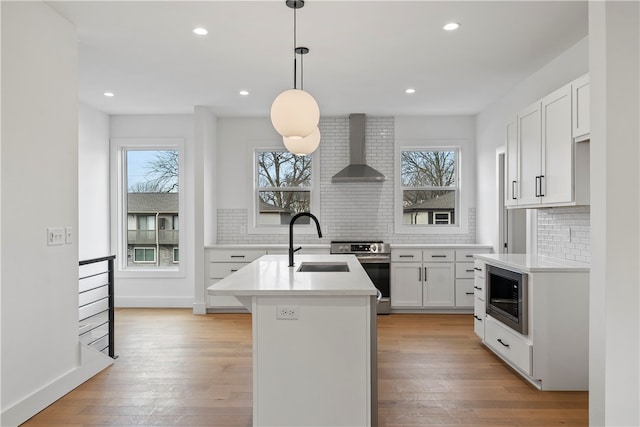 kitchen with a kitchen island with sink, a wealth of natural light, stainless steel appliances, and wall chimney range hood