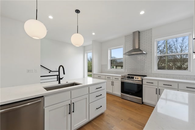 kitchen with light hardwood / wood-style flooring, stainless steel appliances, white cabinetry, sink, and wall chimney exhaust hood