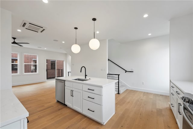 kitchen featuring a kitchen island with sink, light wood-type flooring, stainless steel appliances, hanging light fixtures, and white cabinets