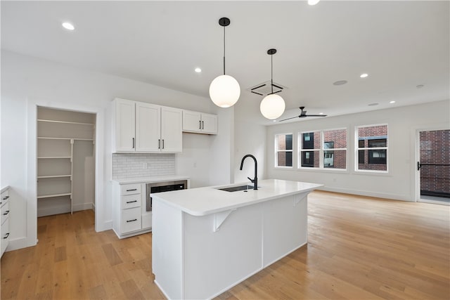 kitchen with decorative light fixtures, light hardwood / wood-style floors, white cabinetry, sink, and a center island with sink