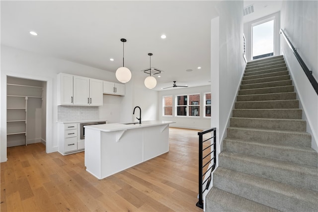 kitchen with light hardwood / wood-style floors, plenty of natural light, a center island with sink, and white cabinetry