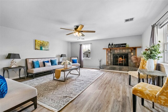 living room with ceiling fan, a tiled fireplace, and hardwood / wood-style floors