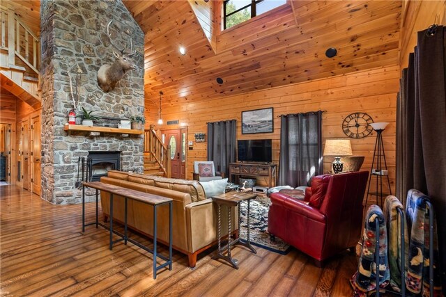 living room featuring a stone fireplace, high vaulted ceiling, hardwood / wood-style flooring, and wooden walls