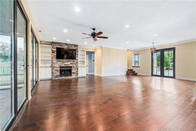 unfurnished living room with built in features, ceiling fan, dark hardwood / wood-style floors, and a stone fireplace