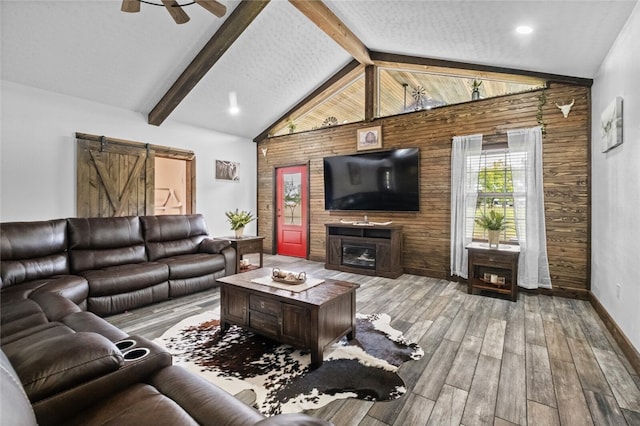 living room with wooden walls, high vaulted ceiling, a barn door, ceiling fan, and light wood-type flooring