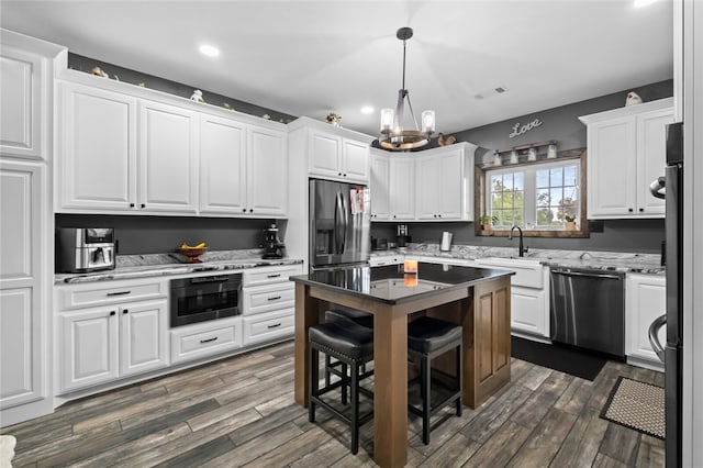 kitchen with appliances with stainless steel finishes, a notable chandelier, white cabinetry, sink, and dark wood-type flooring