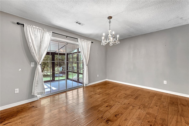 empty room with a textured ceiling, an inviting chandelier, and hardwood / wood-style floors