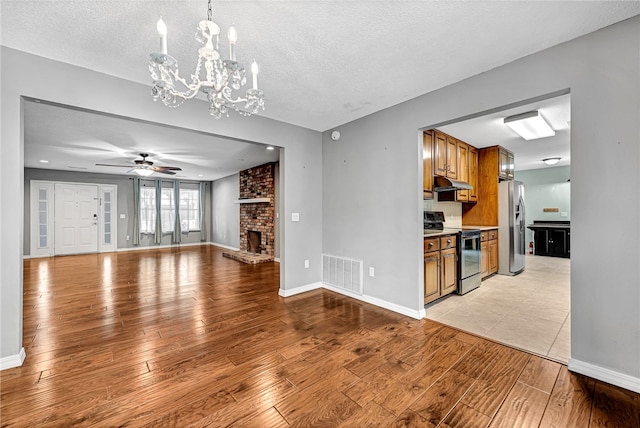 living room with light wood-type flooring, ceiling fan with notable chandelier, and a textured ceiling