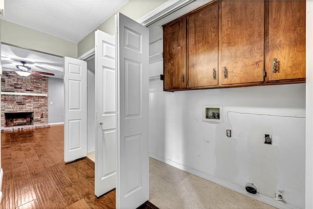 laundry area with hookup for a washing machine, a fireplace, light wood-type flooring, ceiling fan, and cabinets