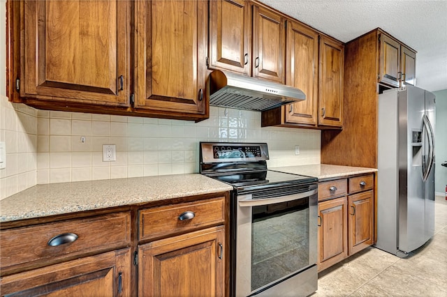 kitchen with a textured ceiling, backsplash, light tile patterned floors, light stone countertops, and appliances with stainless steel finishes