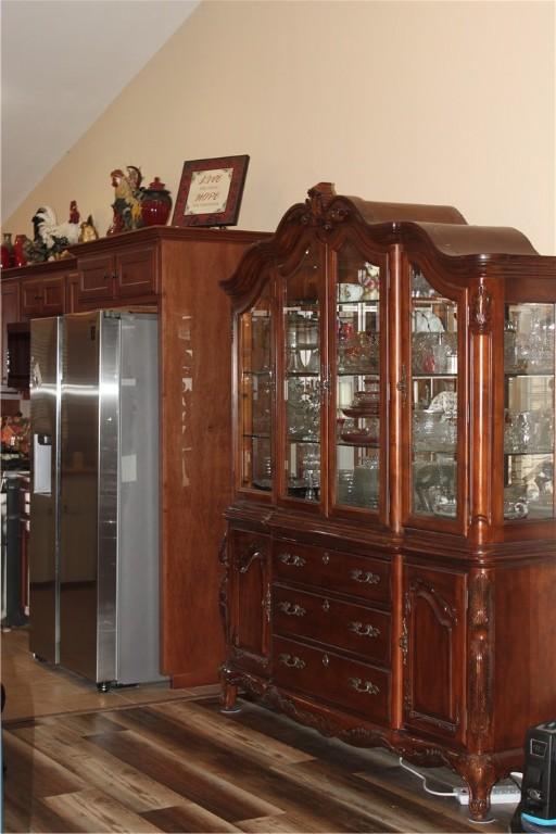 interior space featuring stainless steel fridge with ice dispenser, vaulted ceiling, hardwood / wood-style flooring, and black range