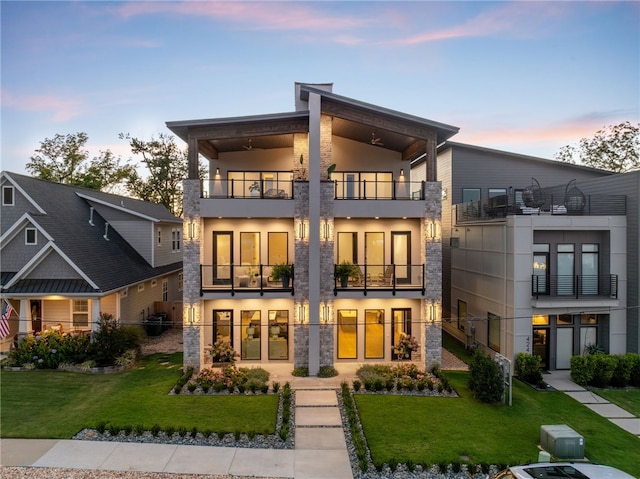 back house at dusk featuring a yard and a balcony