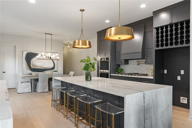 kitchen with decorative light fixtures, light stone countertops, light hardwood / wood-style floors, a center island, and a breakfast bar