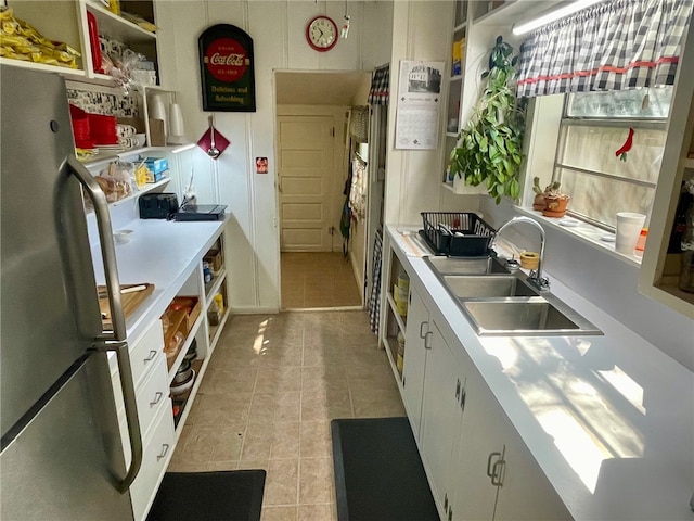 kitchen with light tile patterned flooring, white cabinetry, stainless steel refrigerator, and sink