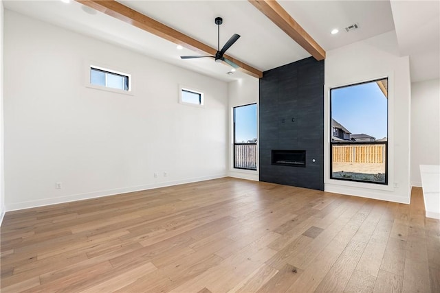 unfurnished living room with ceiling fan, a large fireplace, light wood-type flooring, and beam ceiling