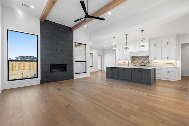 kitchen featuring beam ceiling, hanging light fixtures, light hardwood / wood-style flooring, a center island with sink, and white cabinets