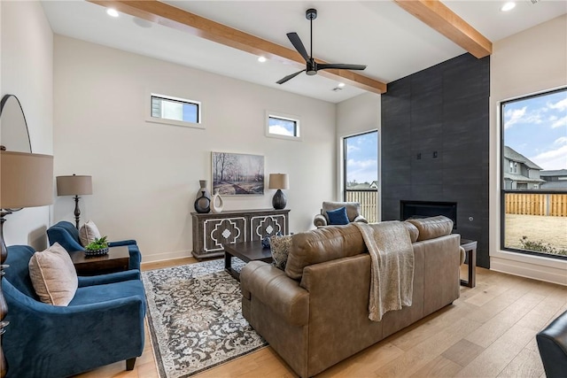 living room with beamed ceiling, ceiling fan, a fireplace, and light hardwood / wood-style flooring