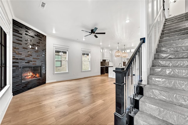 staircase featuring ceiling fan with notable chandelier, wood-type flooring, sink, crown molding, and a fireplace