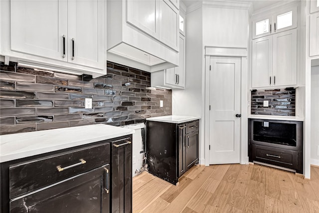 kitchen with white cabinetry, light stone counters, ornamental molding, light hardwood / wood-style flooring, and decorative backsplash