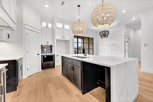 kitchen with decorative light fixtures, a notable chandelier, sink, an island with sink, and white cabinets