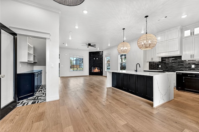 kitchen with a center island with sink, crown molding, white cabinetry, hanging light fixtures, and light hardwood / wood-style flooring