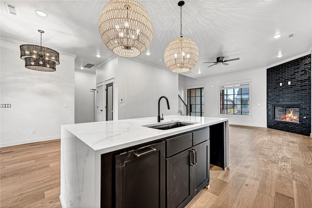 kitchen featuring a center island with sink, sink, decorative light fixtures, and light hardwood / wood-style flooring