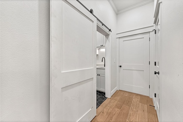 hallway with a barn door, light hardwood / wood-style flooring, and crown molding