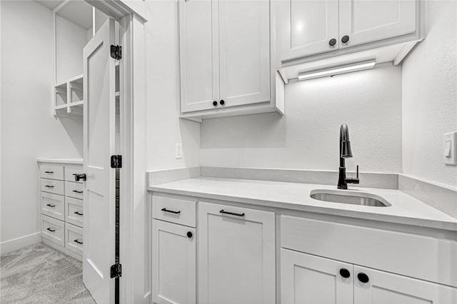 kitchen with sink, light colored carpet, and white cabinets