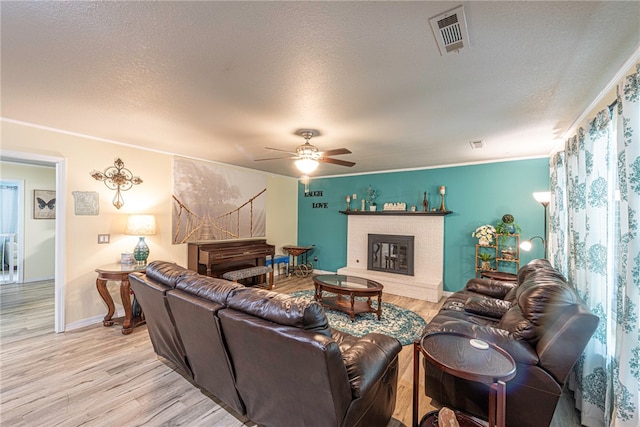 living room with ceiling fan, a textured ceiling, light wood-type flooring, and ornamental molding