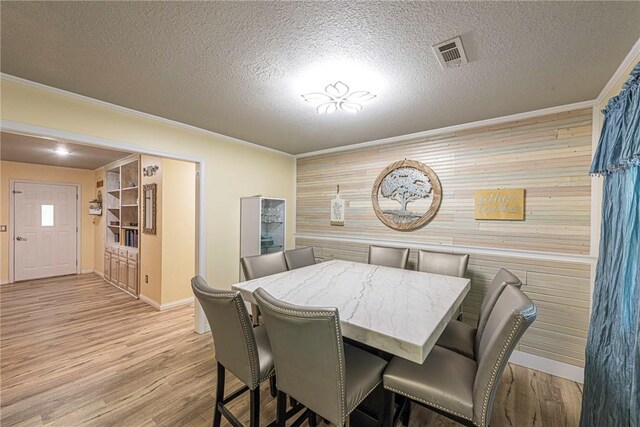 dining area featuring ornamental molding, wooden walls, a textured ceiling, and light wood-type flooring