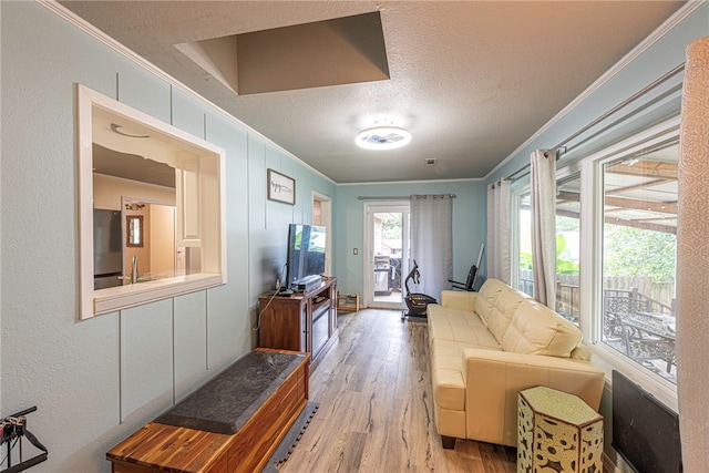 living room with light wood-type flooring, a textured ceiling, and crown molding