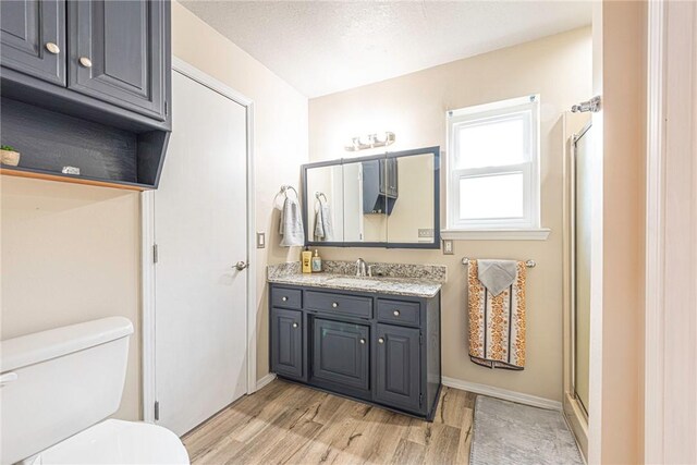 bathroom with vanity, a textured ceiling, a shower with shower door, hardwood / wood-style flooring, and toilet