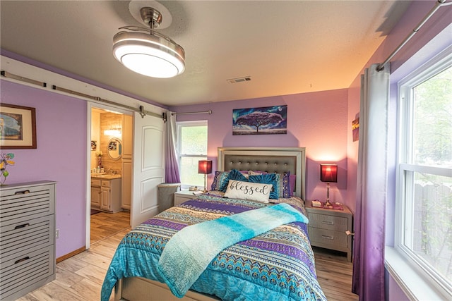 bedroom with light wood-type flooring, connected bathroom, a barn door, and multiple windows