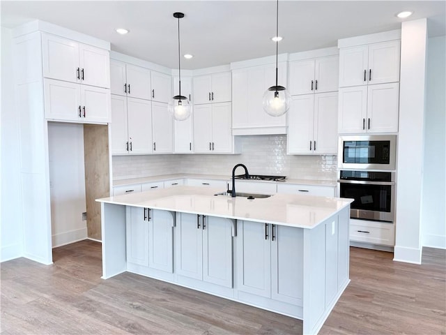 kitchen with an island with sink, decorative light fixtures, white cabinetry, and stainless steel oven