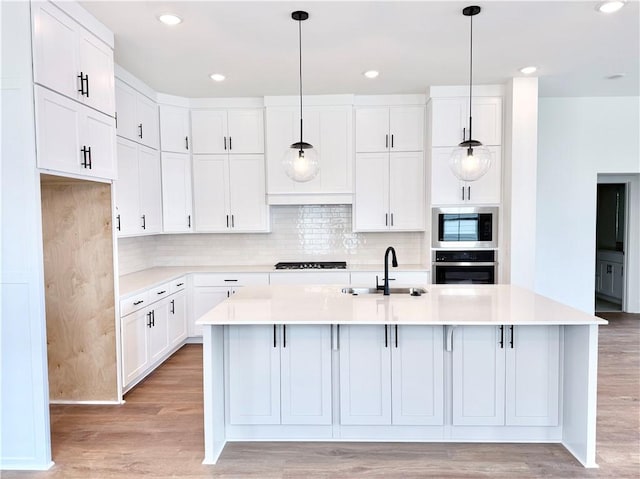 kitchen with built in microwave, a kitchen island with sink, stainless steel oven, and sink