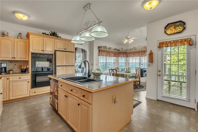 kitchen with double oven, a kitchen island with sink, sink, light brown cabinets, and pendant lighting