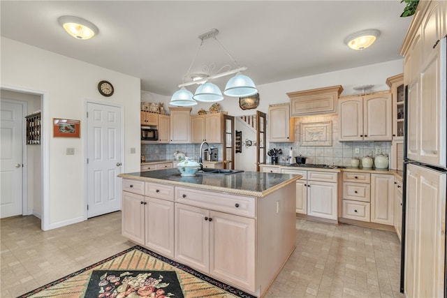 kitchen featuring backsplash, built in appliances, a kitchen island with sink, and light brown cabinetry