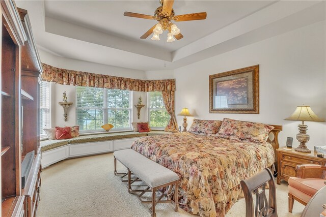 bedroom with a tray ceiling, ceiling fan, and light carpet